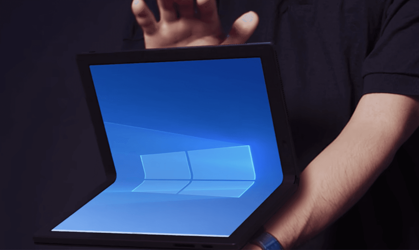 Hands holding an open foldable PC showing a blue desktop wallpaper