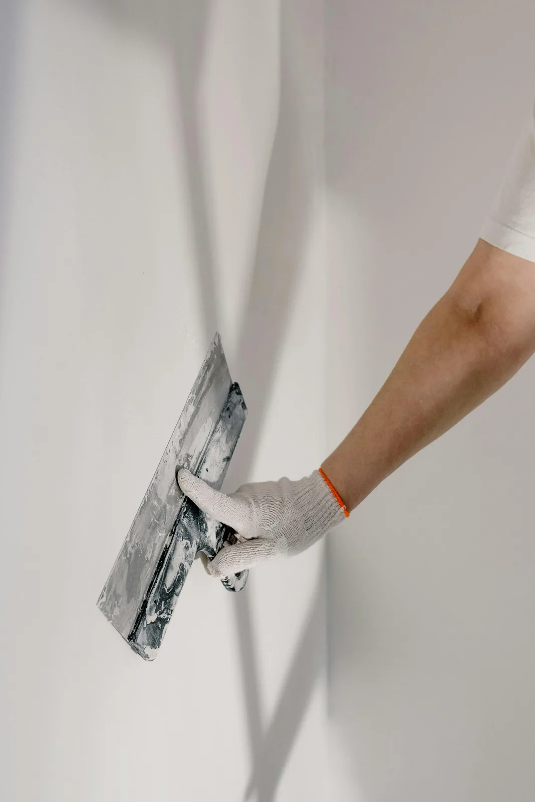 Worker skimming white plaster on wall with wide trowel