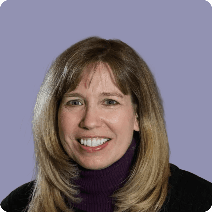 A smiling woman in a black sweater in front of a purple background