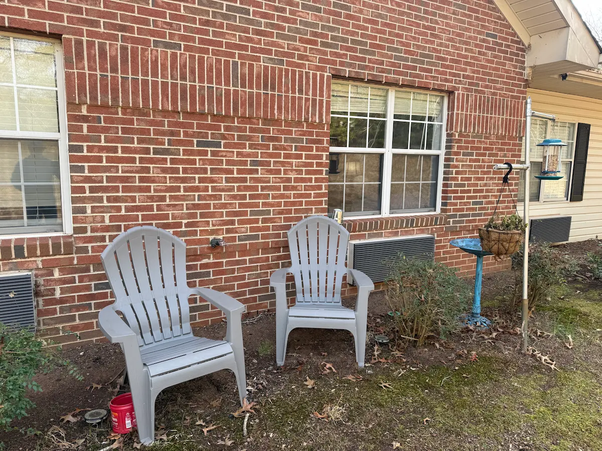 Two plastic chairs sitting against a brick building, suggesting a simple, quiet place to sit and reflect.