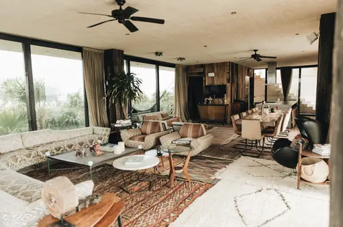 Large Casa Sastran living room connecting to dining area, featuring TV, ceiling fans, and green views.