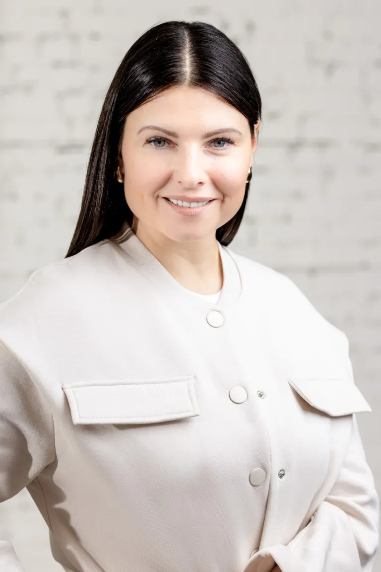 Image of Woman smiling in white jacket standing in front of a textured white background at KHD Homes.