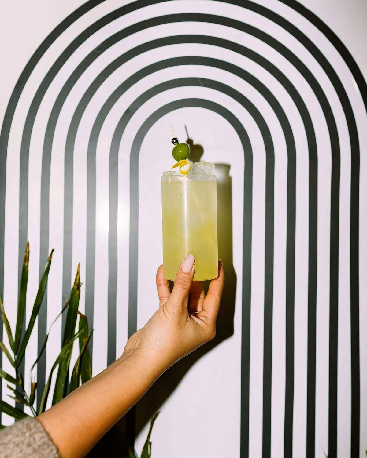 A stylish cocktail featuring a garnish of green grapes held up against a bold black-and-white geometric backdrop at Node Studio, showcasing creative and modern design elements