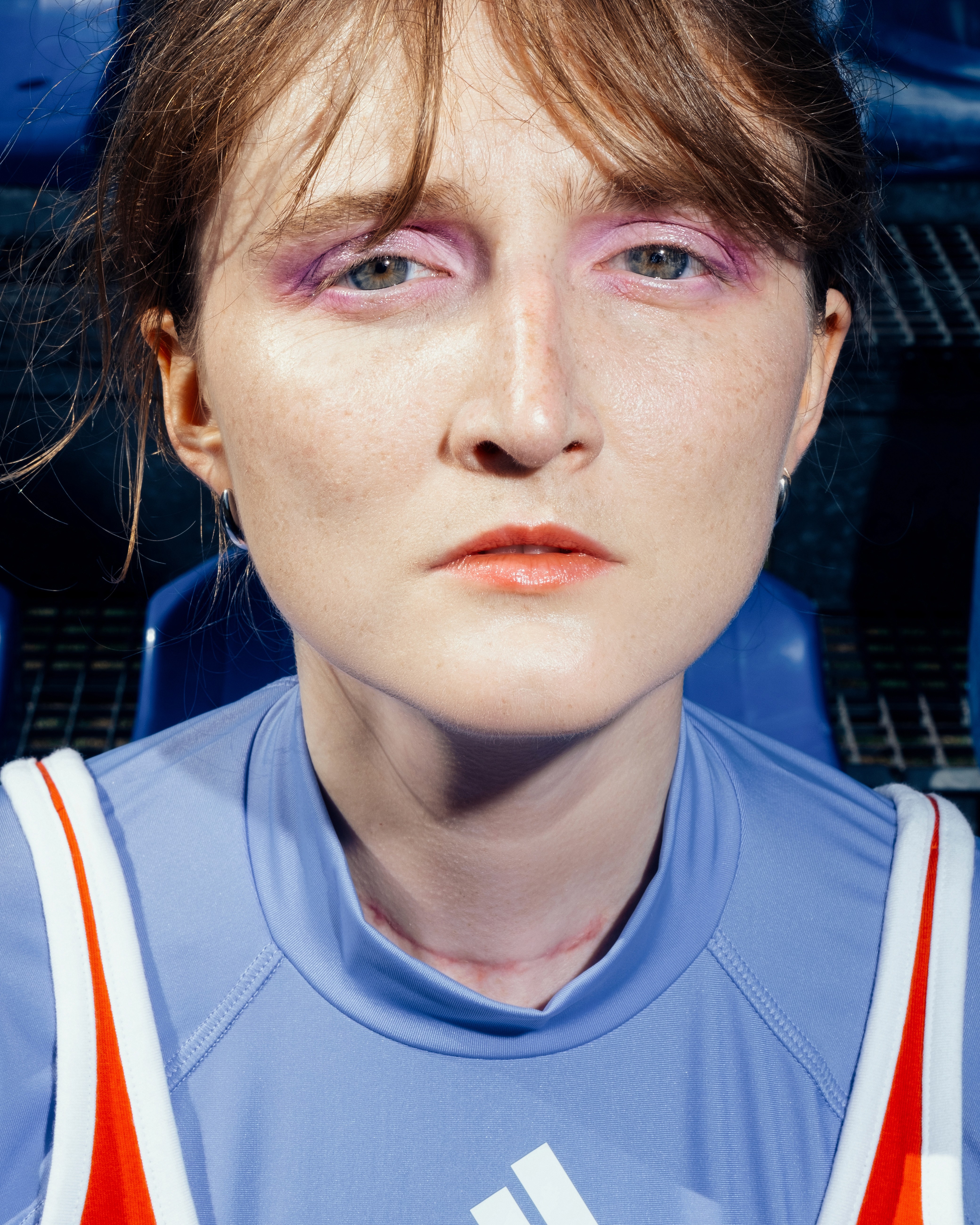 Close-up of a person with purple eye makeup in athletic clothing, staring seriously into the lens.