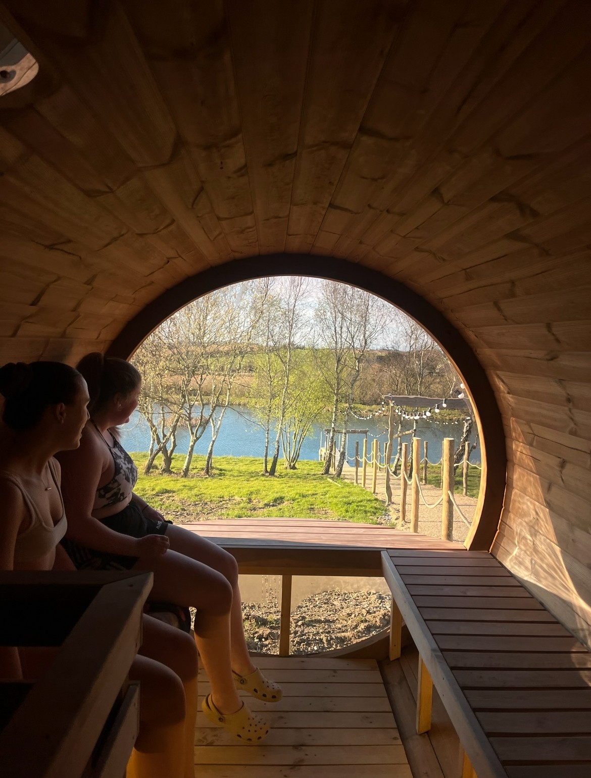 A smiling young man with crossed arms, wearing a plaid shirt and white t-shirt, poses against a dark background.