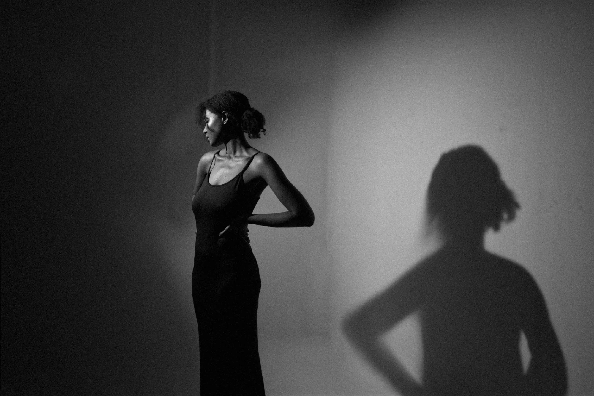 A black and white photograph of a woman lit by a spotlight in studio by Acquille Dunkley.
