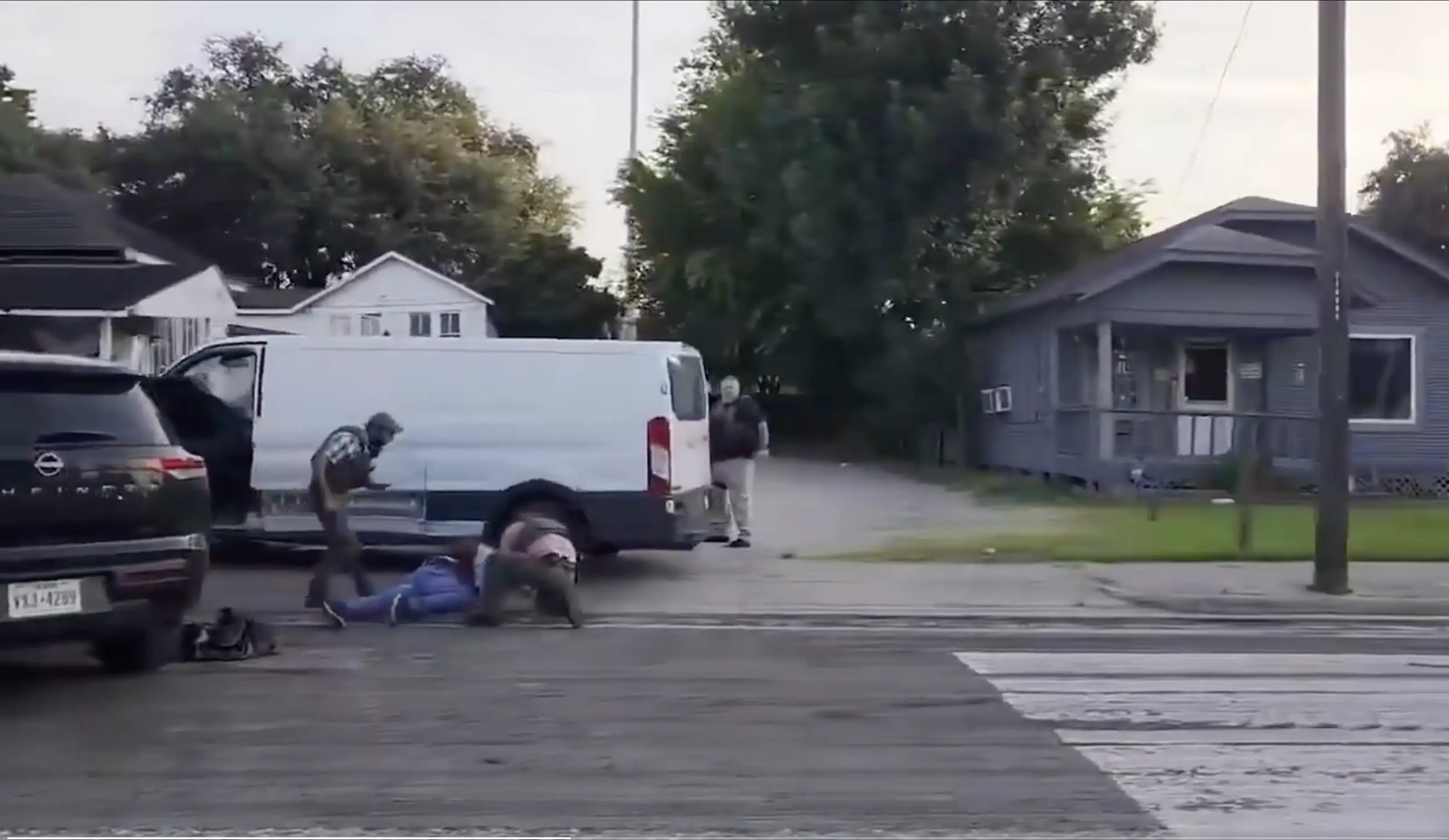 Law enforcement officers detain a person during an immigration enforcement operation in a residential neighborhood.