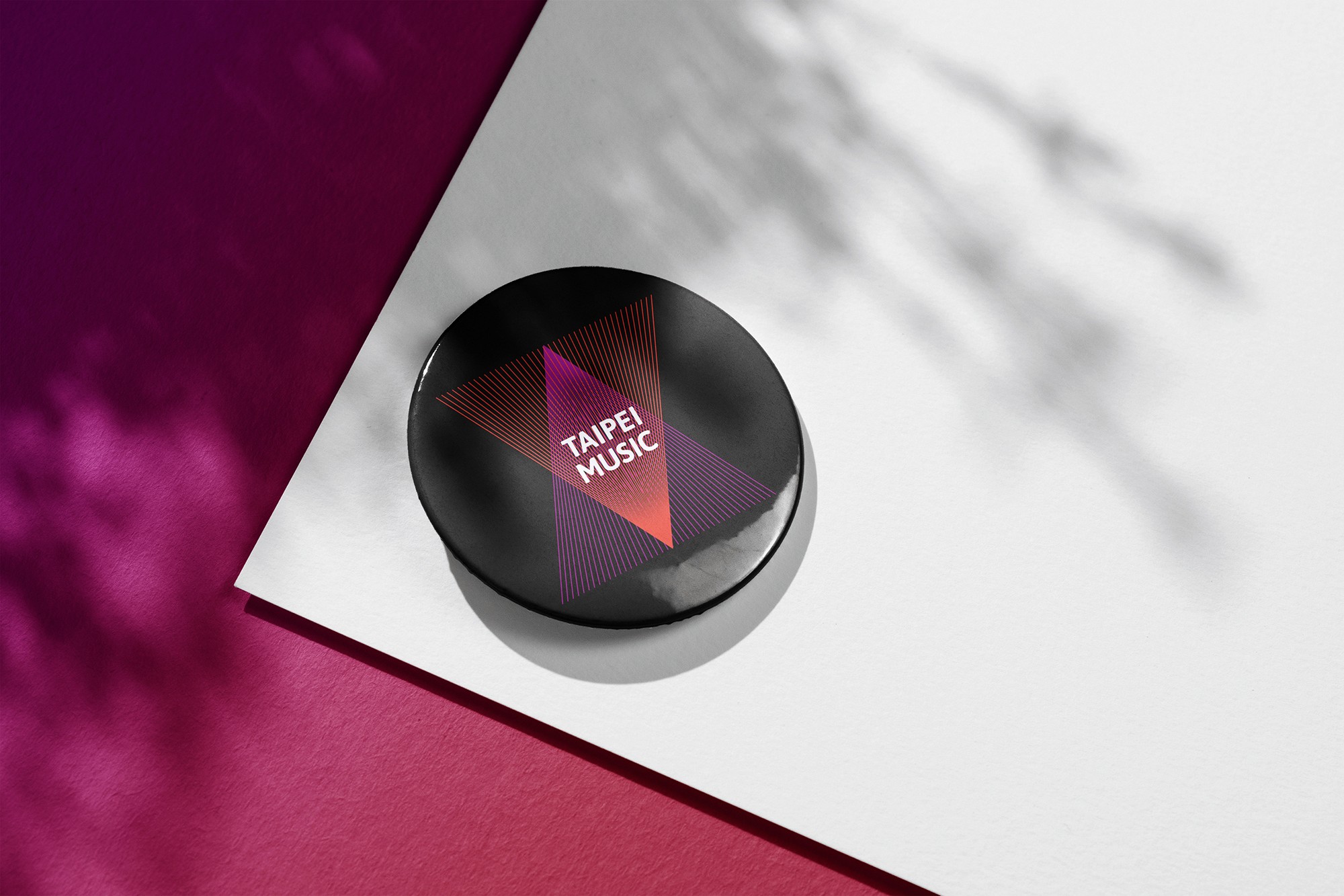 這張圖像展示了台北音樂的圓形徽章，徽章上有紫紅色漸層三角形的圖形和 "Taipei Music" 字樣的品牌識別，背景是紫色和白色的紙張。