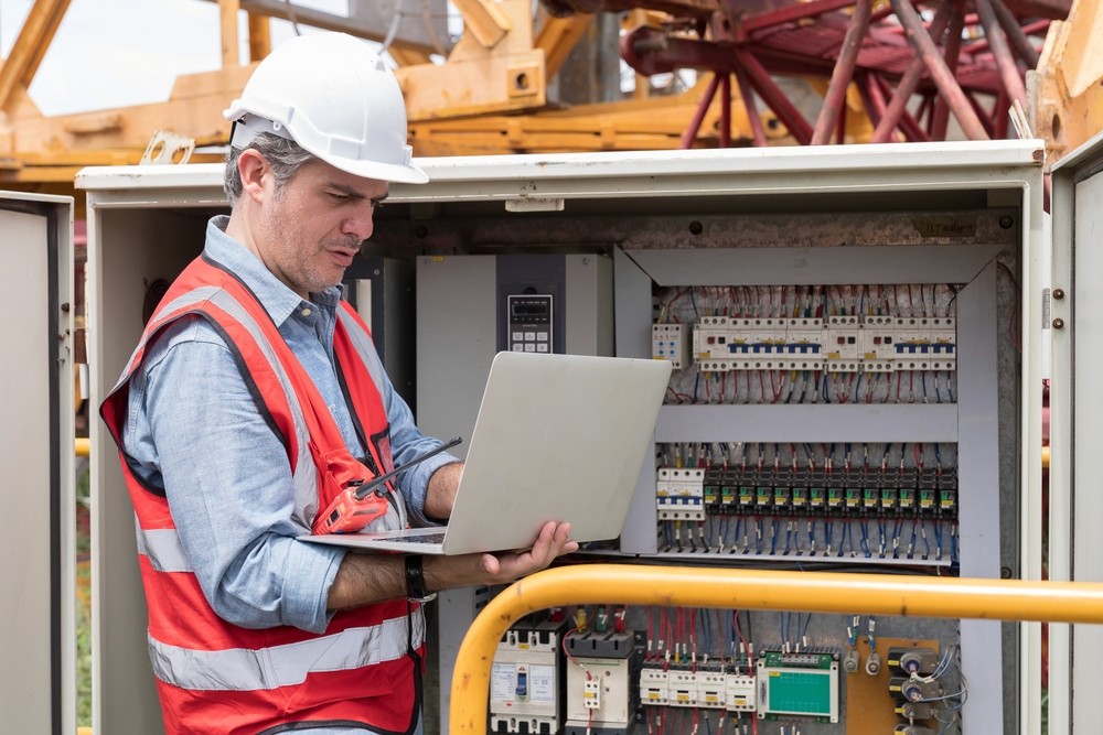 Male electrician checking, repair, maintenance operation electric system in crane construction. Male electrician using laptop computer working with operation electric system in construction site