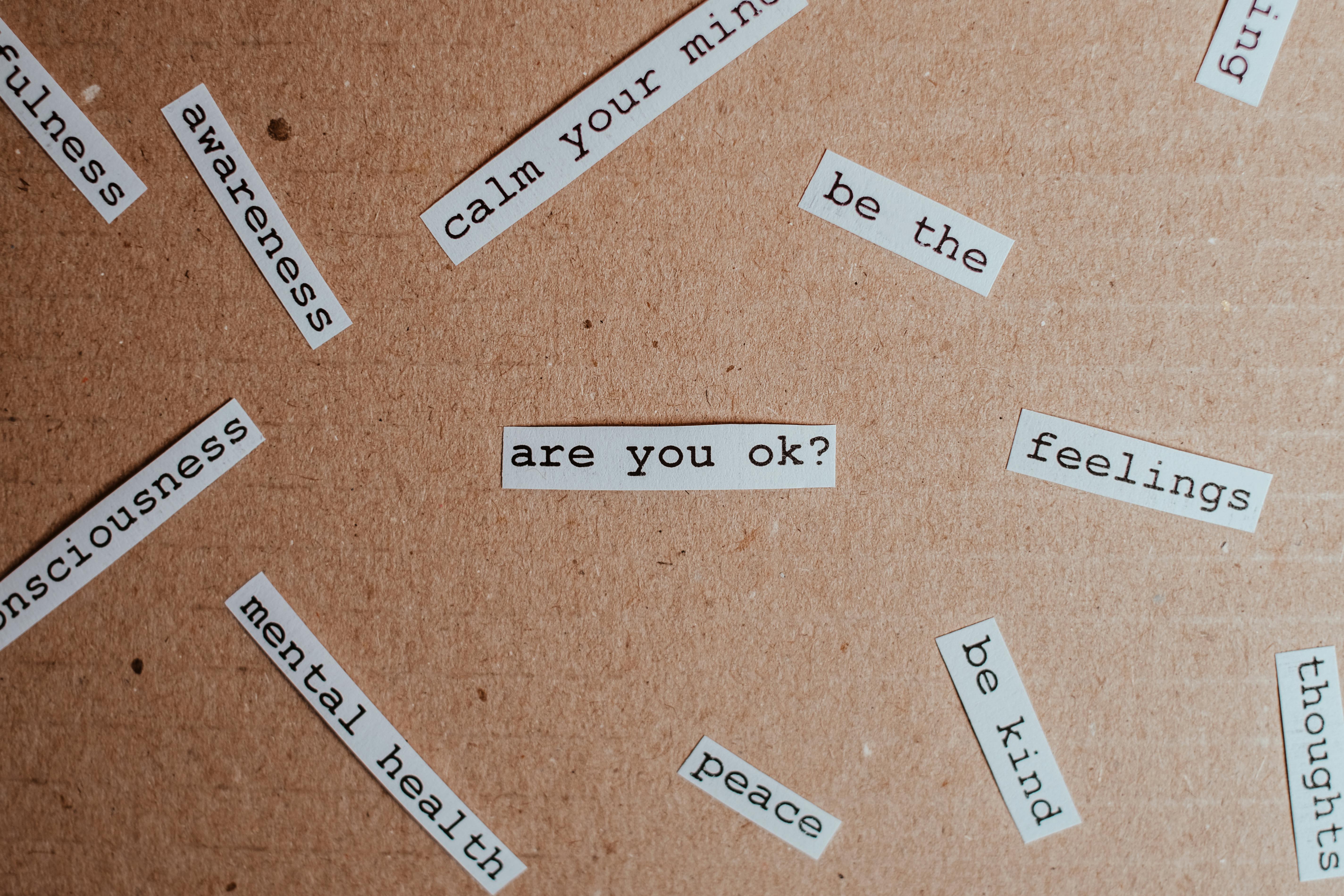 Parole stampate su cartoncino con termini come “are you ok?”, “mental health” e “awareness”, simbolo di consapevolezza emotiva e salute mentale.