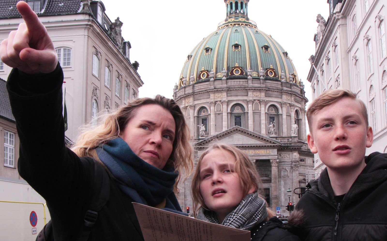 Mystery hunt participants at Amalienborg Palace, Copenhagen, pointing towards a landmark.