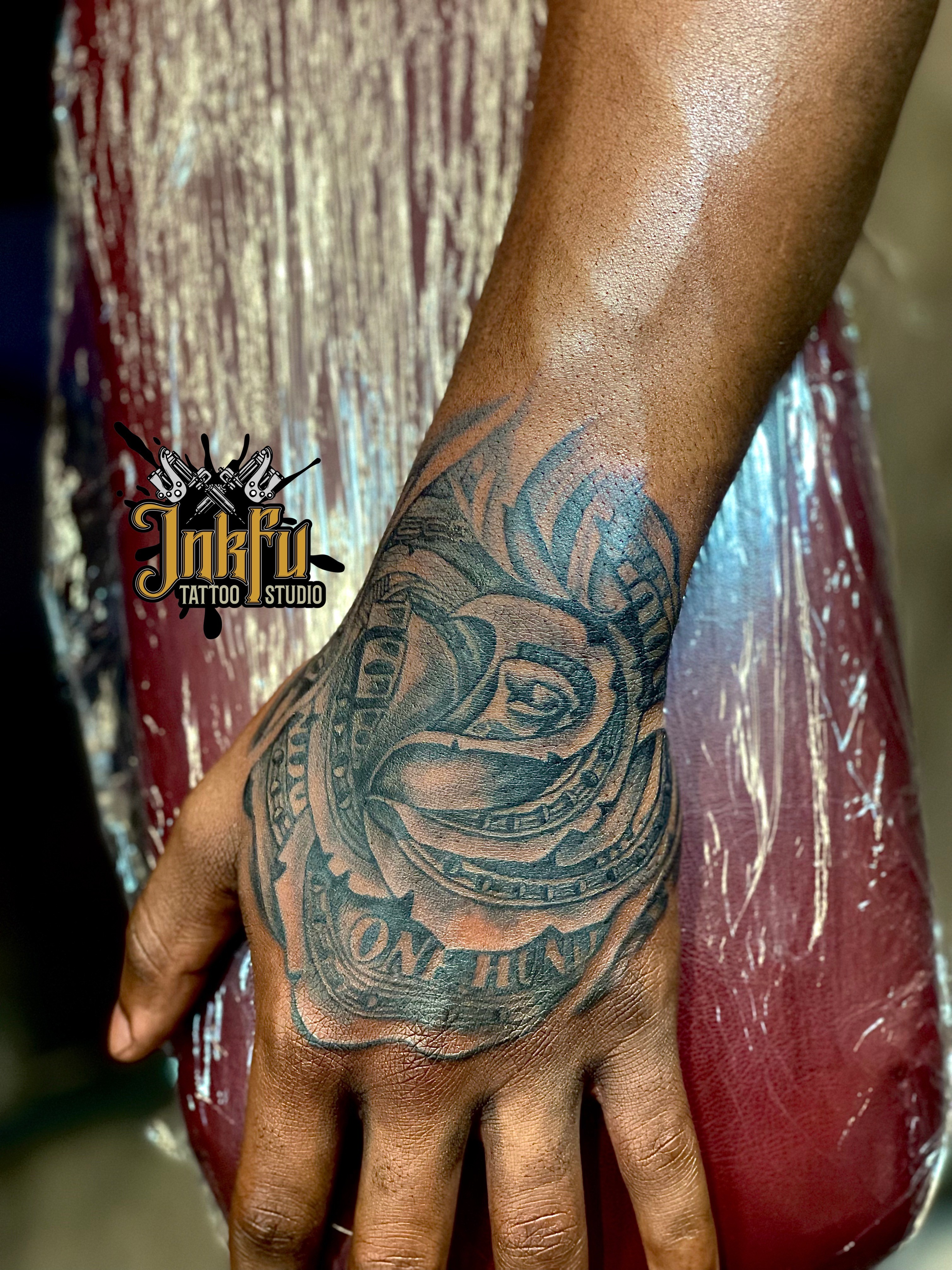 Black and grey rose formed from a rolled hundred-dollar bill, hand tattoo by Meer Rich