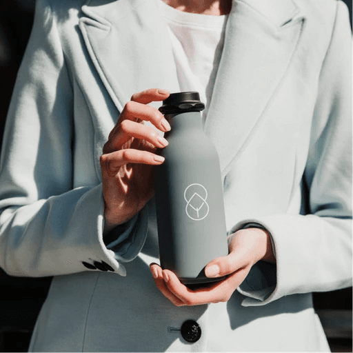 Person holding a reusable water bottle wearing a light grey coat.