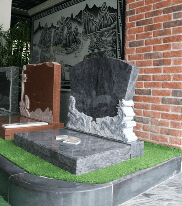 A black granite tombstone with intricate carvings of dragon motifs at the base. The tombstone rests on an elevated platform surrounded by artificial grass, creating a serene and respectful display.