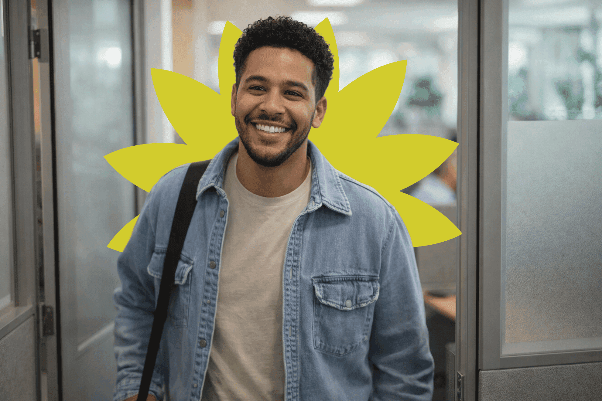 A smiling person wearing a denim jacket is standing in a modern office hallway, with a bright yellow sunflower design in the background, suggesting a cheerful and welcoming atmosphere.