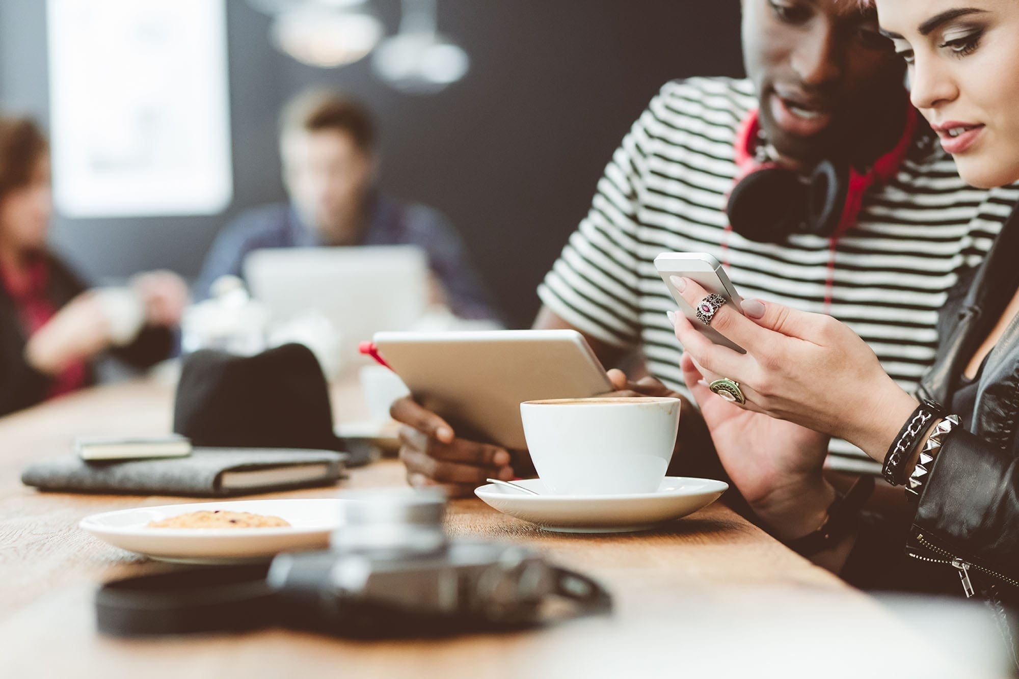 Two friends in a café using a tablet and a phone