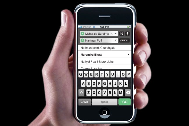 A hand holds a black iPhone displaying a screen showing a web browser. The screen shows a list of names: "Maharaja Surajmal" and "Nariman Poll," along with "Narendra Bhatt" and "Nariyal Paani Store, Juhu." The time displayed is 4:20 PM. The phone's carrier is 33, and the battery is at 85%. The screen also shows "QWERTY" on the keyboard and "space" and "GO" buttons at the bottom.