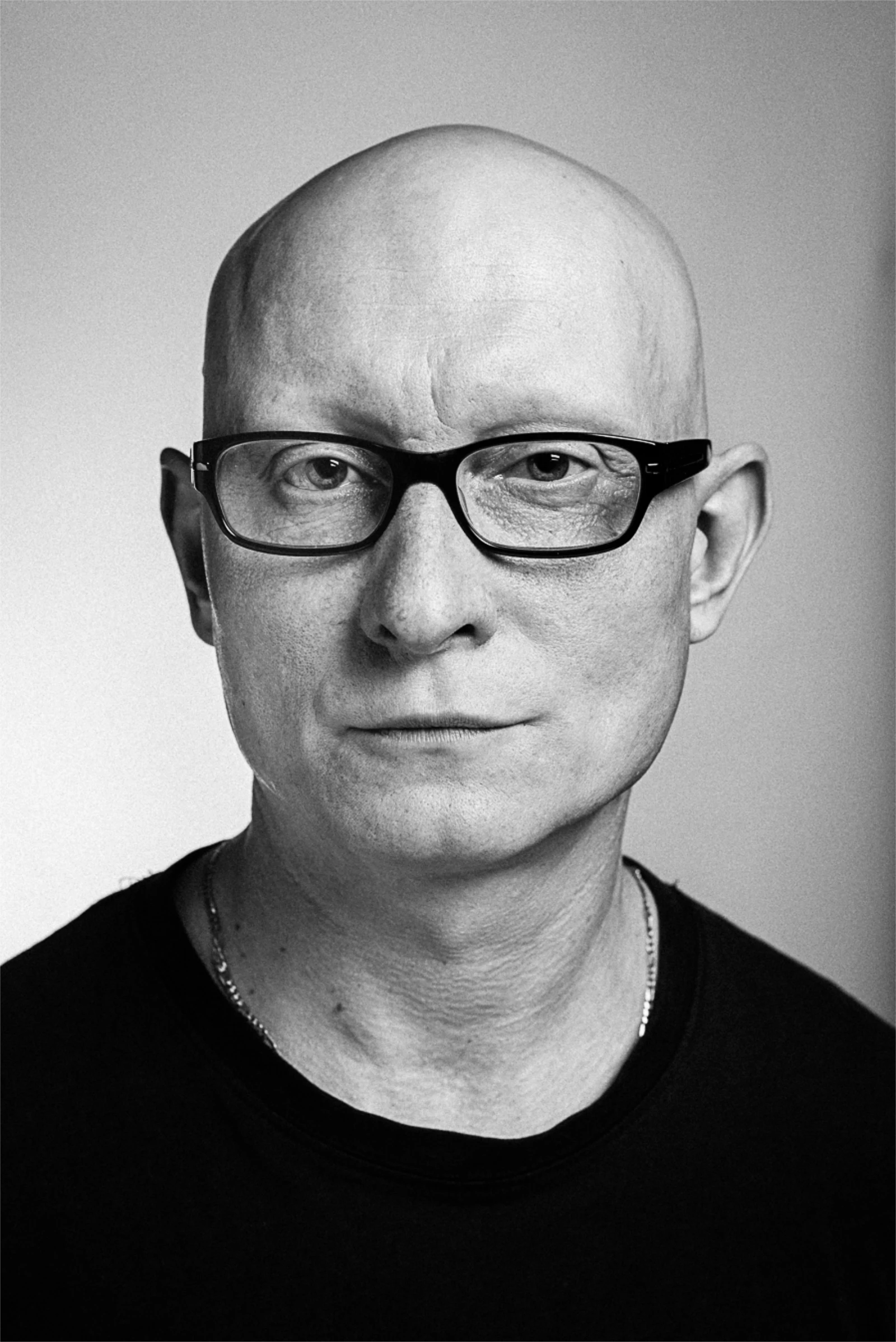 Portret łysego mężczyzny w okularach patrzącego prosto w obiektyw.