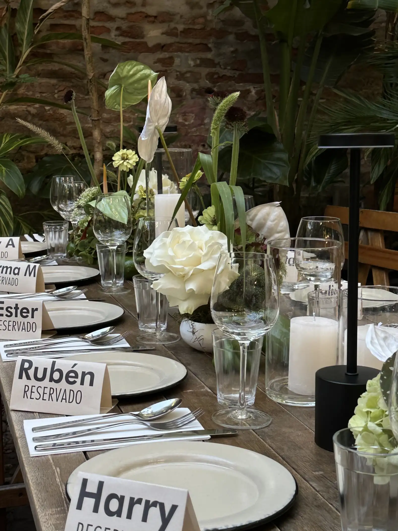 Mesa larga con vajilla blanca y centros florales verdes y blancos, acompañada de velas y carteles de lugares reservados.