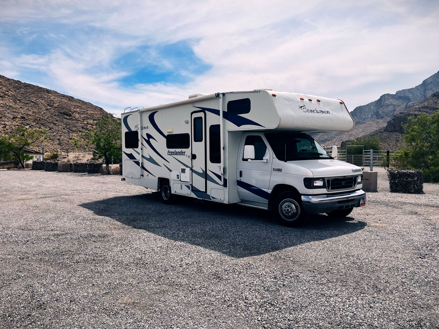 Large white RV parked in the desert with blue skies above.