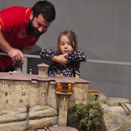 一名留鬍子的男子和一名年輕女孩正觀看一個設於岩石地貌上的古代建築精緻微縮模型。