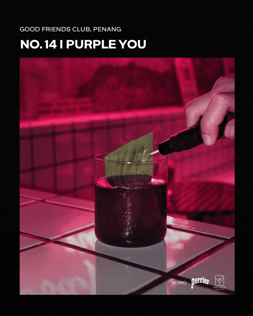 A cocktail named 'I Purple You' served at Good Friends Club in Penang, featuring a glass filled with a dark liquid and a green leaf being torched, set against a pink backdrop.