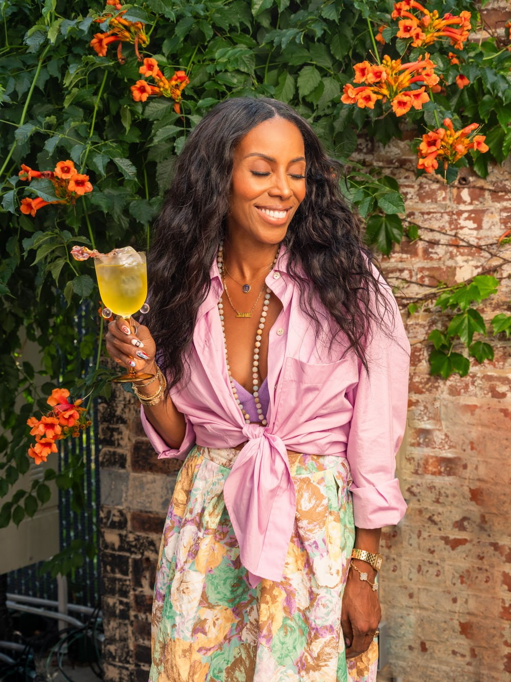 June Ambrose holding a St Germain cocktail beside orange flowers