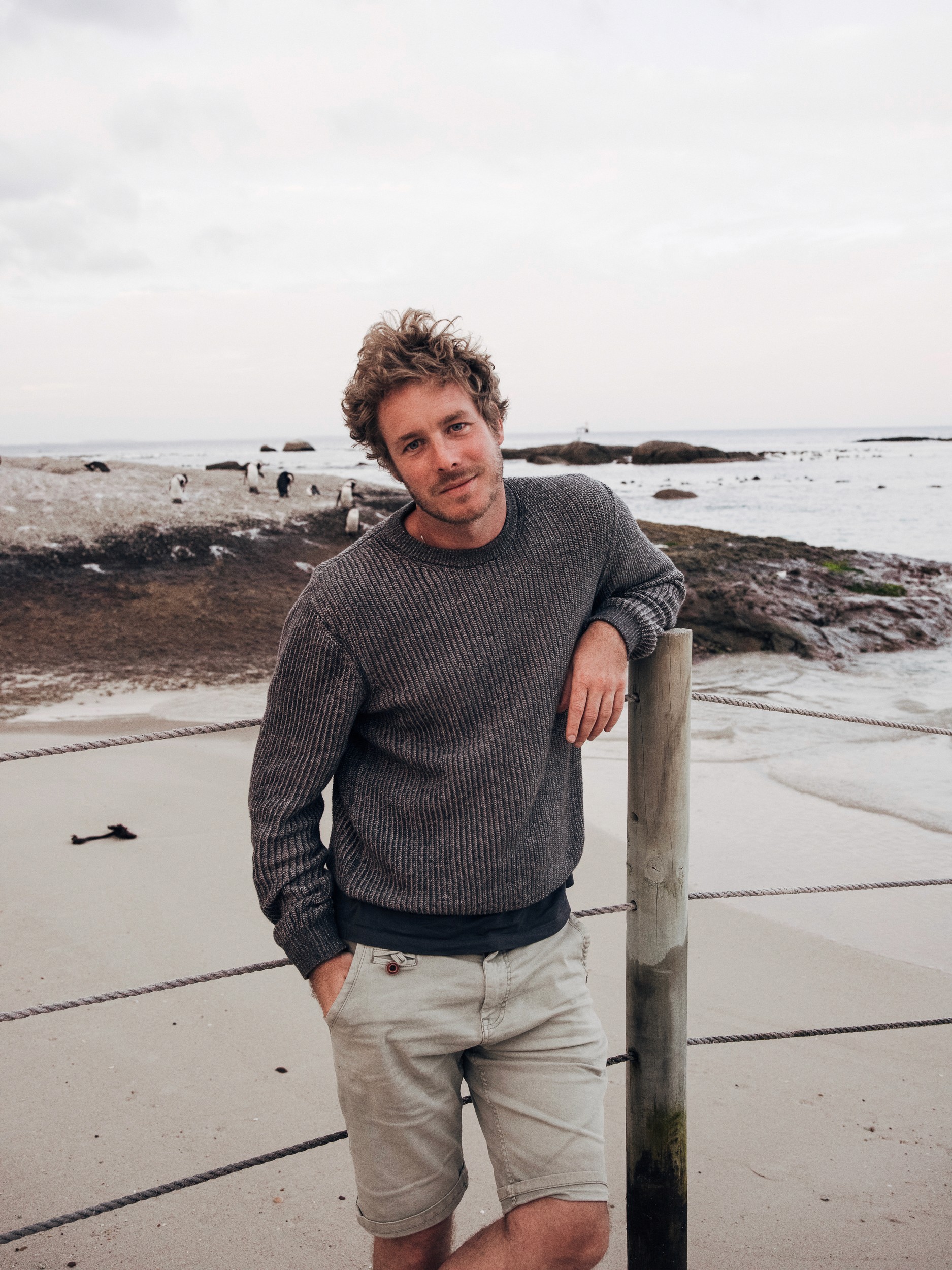 A man with glasses and a brown shirt, crossing his arms.