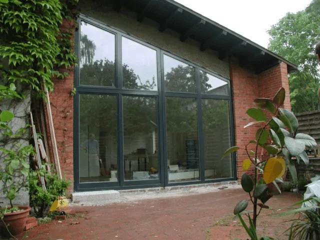 picture showing a wall built with glass from outside the house. the windows are dark framed and down to bottom