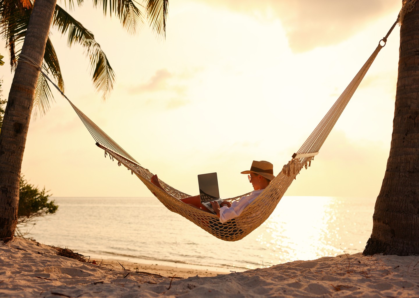 Donna che lavora in smart working all'estero su un'amaca su una spiaggia tropicale