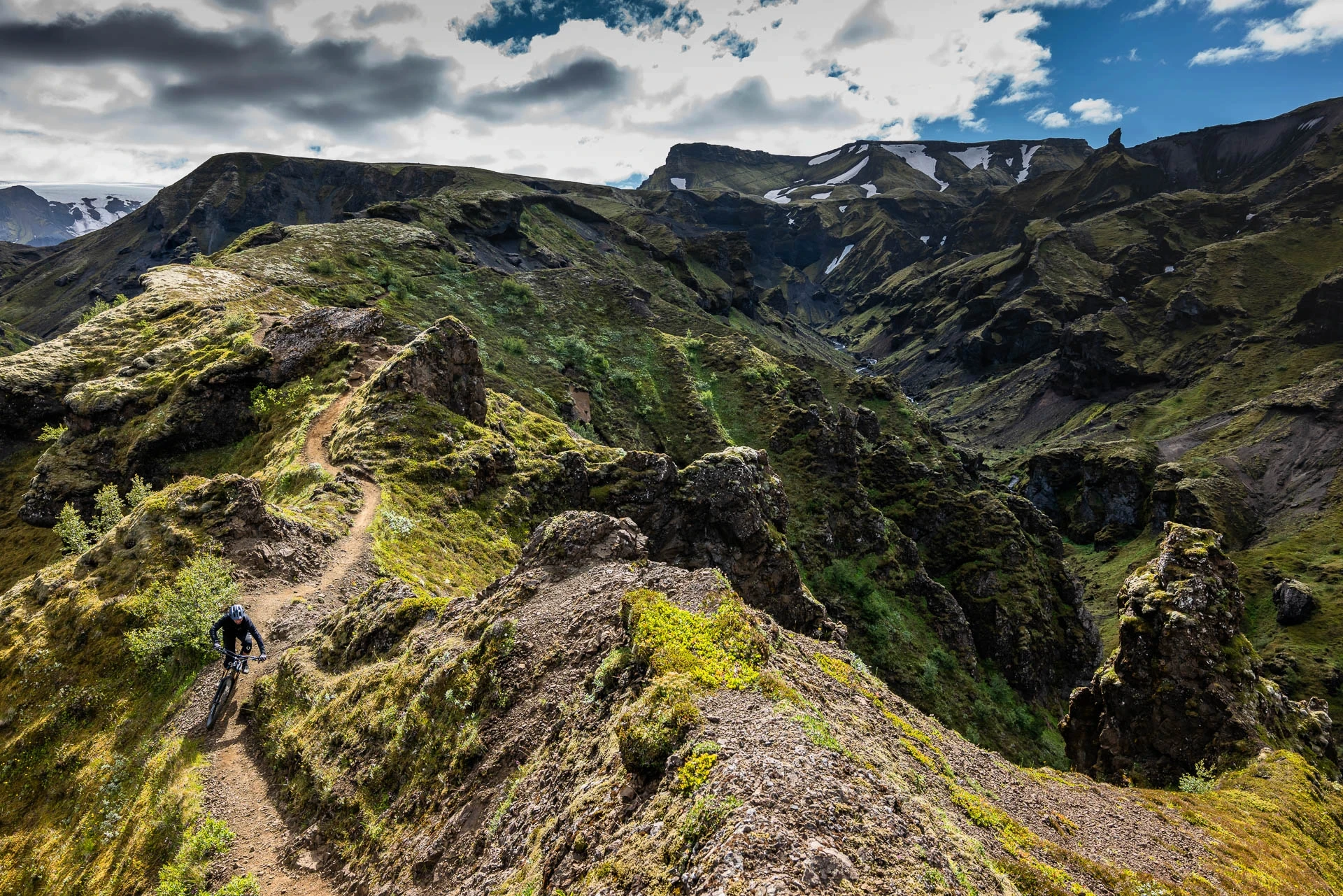 Mountain biker riding singletrack along a ridge above a green canyon.