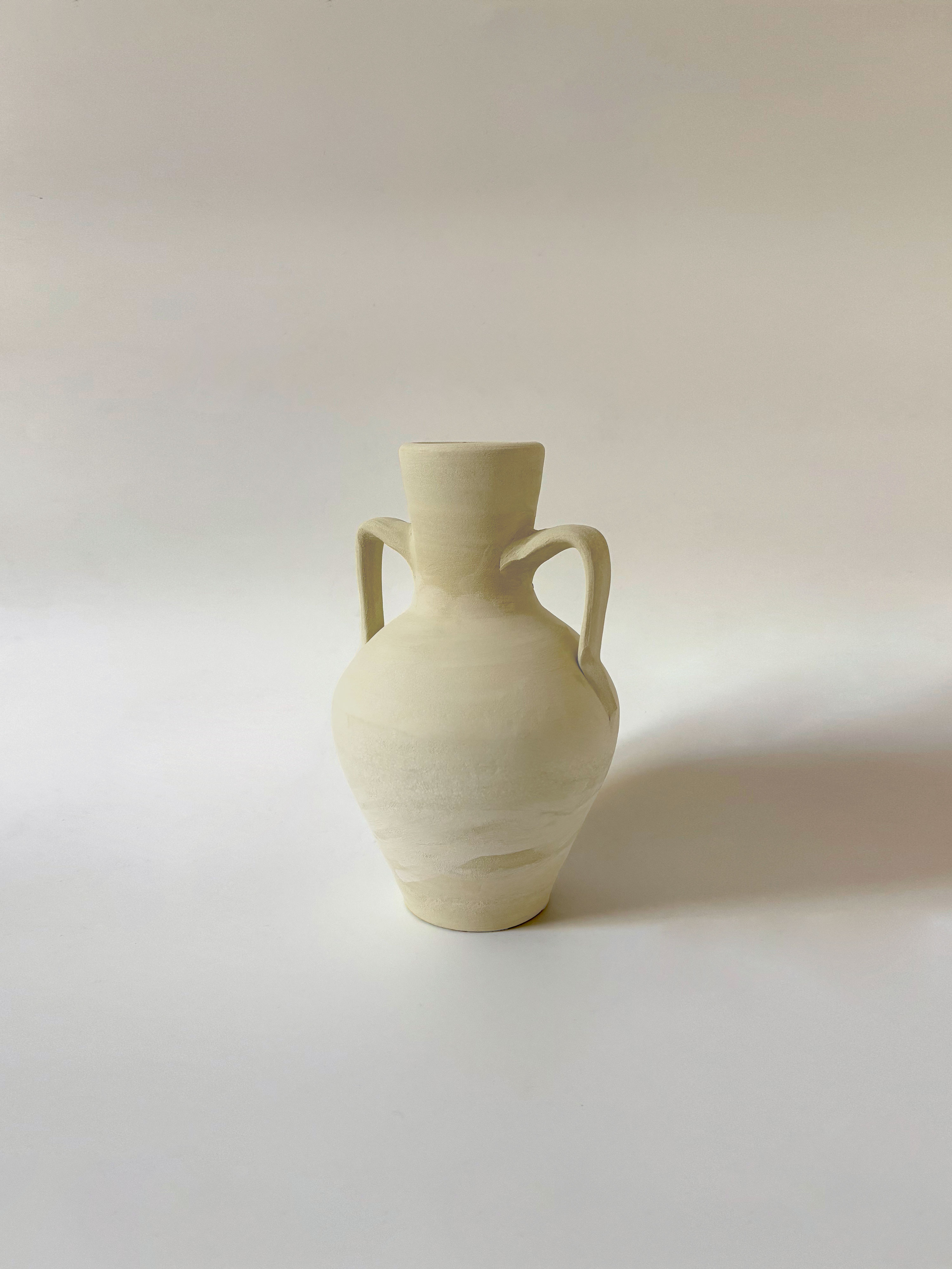 A small, light-colored ceramic vase with two handles, set against a plain white background.