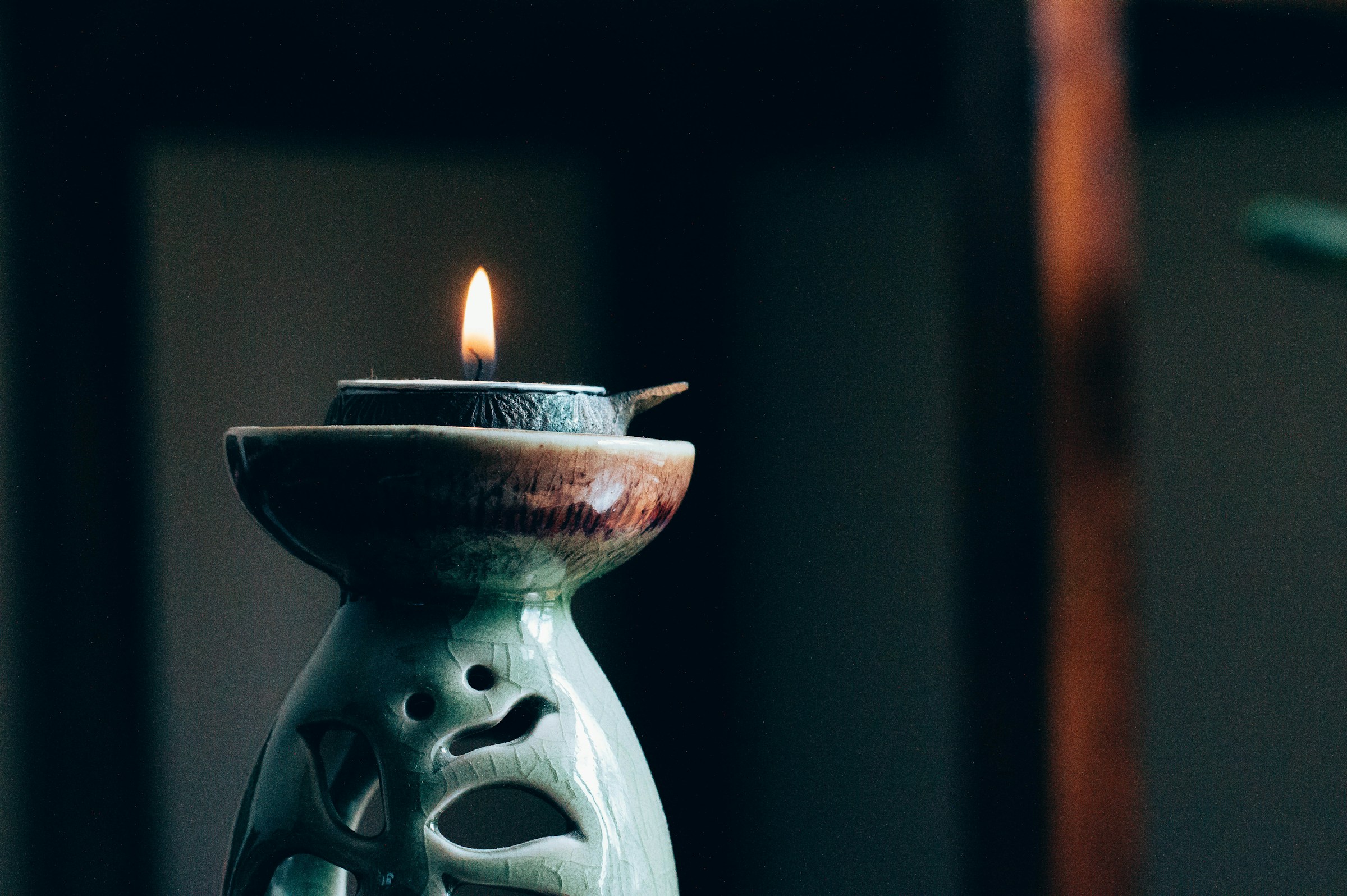 Lit candle on ceramic holder in dimly lit room, creating a serene atmosphere.
