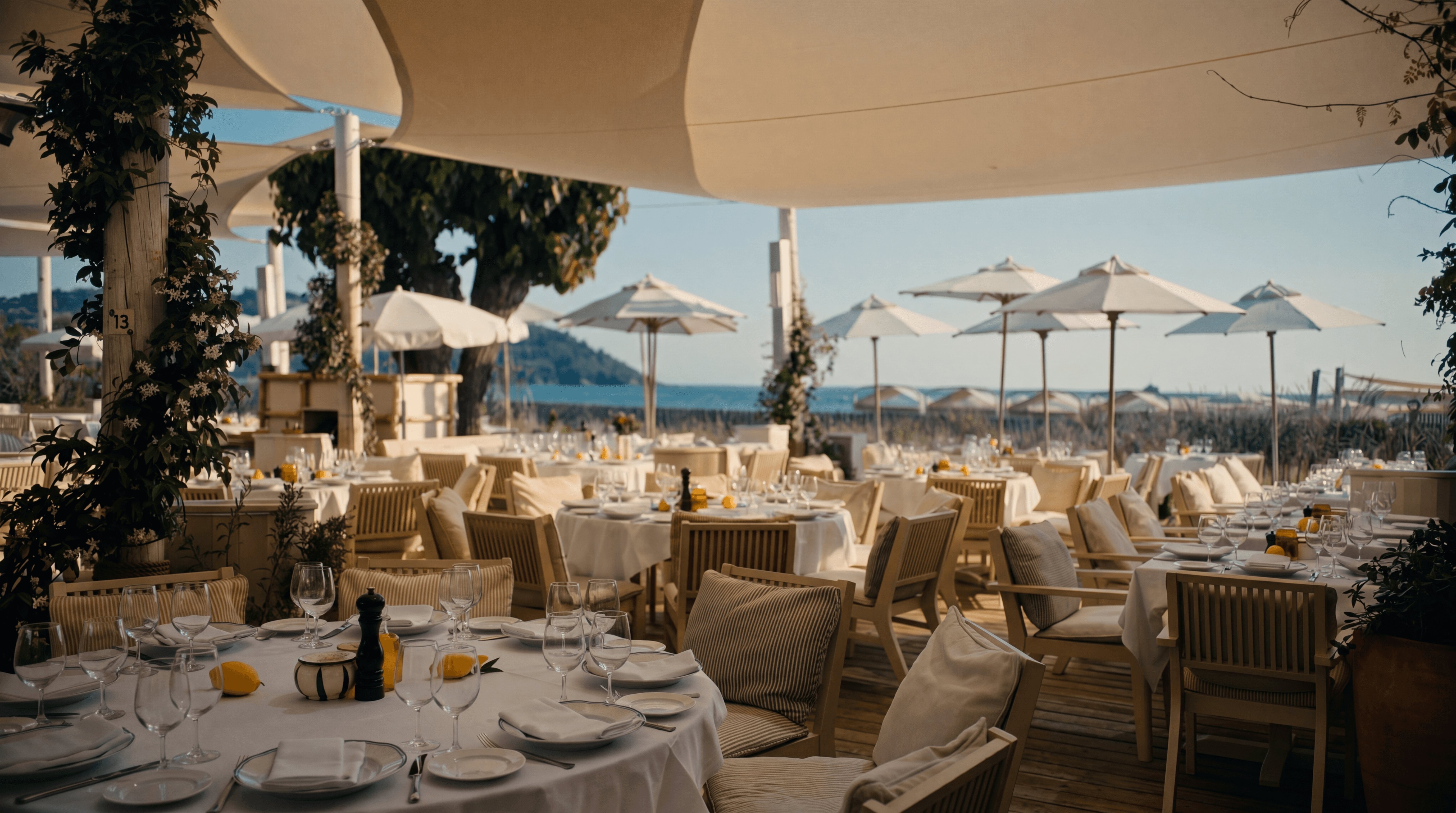 Private dining terrace overlooking the Côte d'Azur coastline at dusk, white linen table set for two with olive branch centrepiece, Riviera sea view