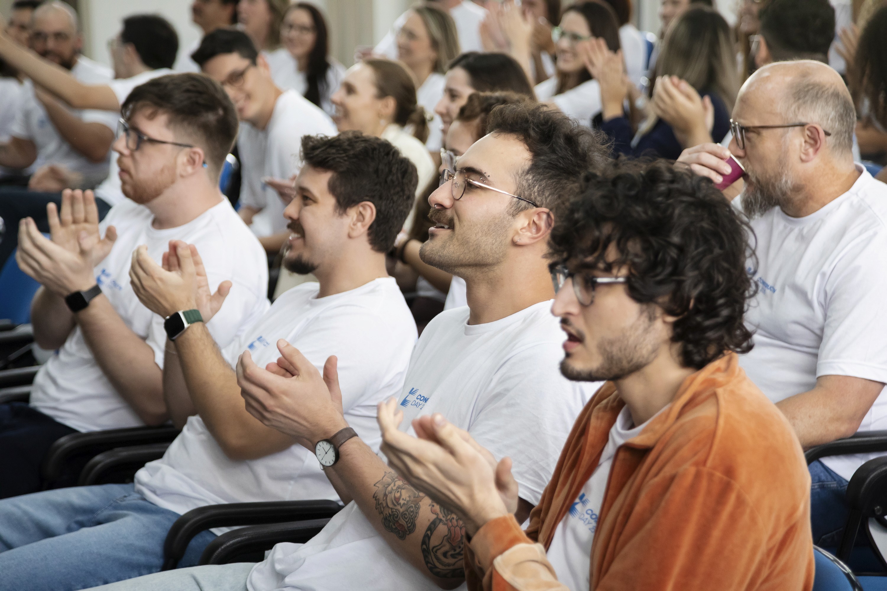 Uma grande foto em grupo com os colaboradores da Construct IN, em um evento interno. Todos estão sorrindo, sentados em um gramado artificial e de pé, com os braços levantados em sinal de entusiasmo e união.