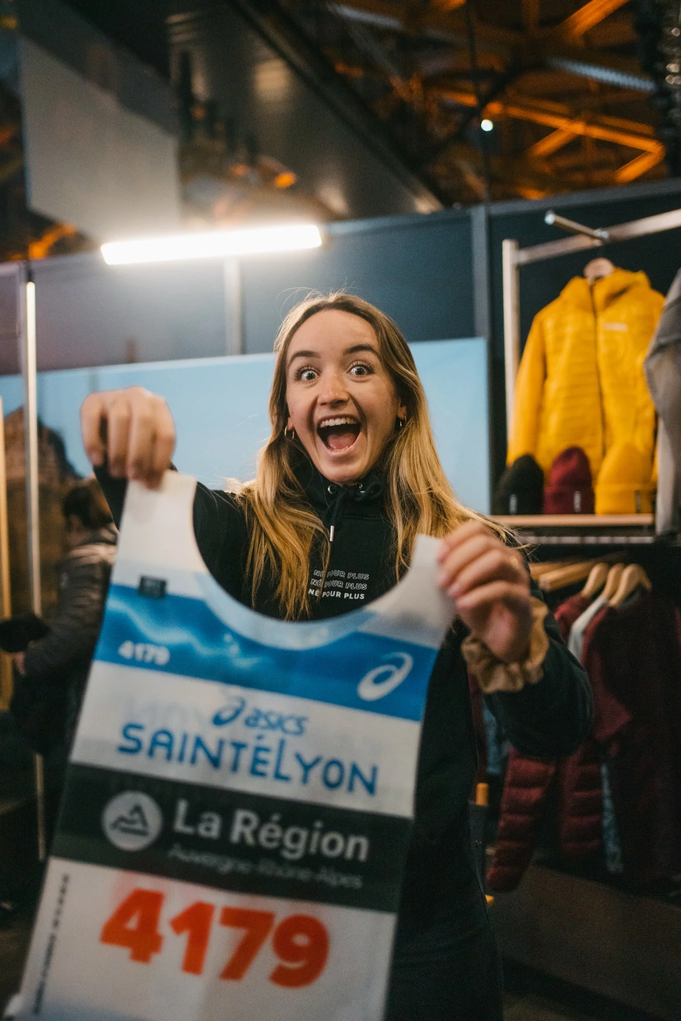 Coureuse enthousiaste présentant son dossard Asics SaintéLyon avant le départ de la course organisée avec Outdoor Perspectives