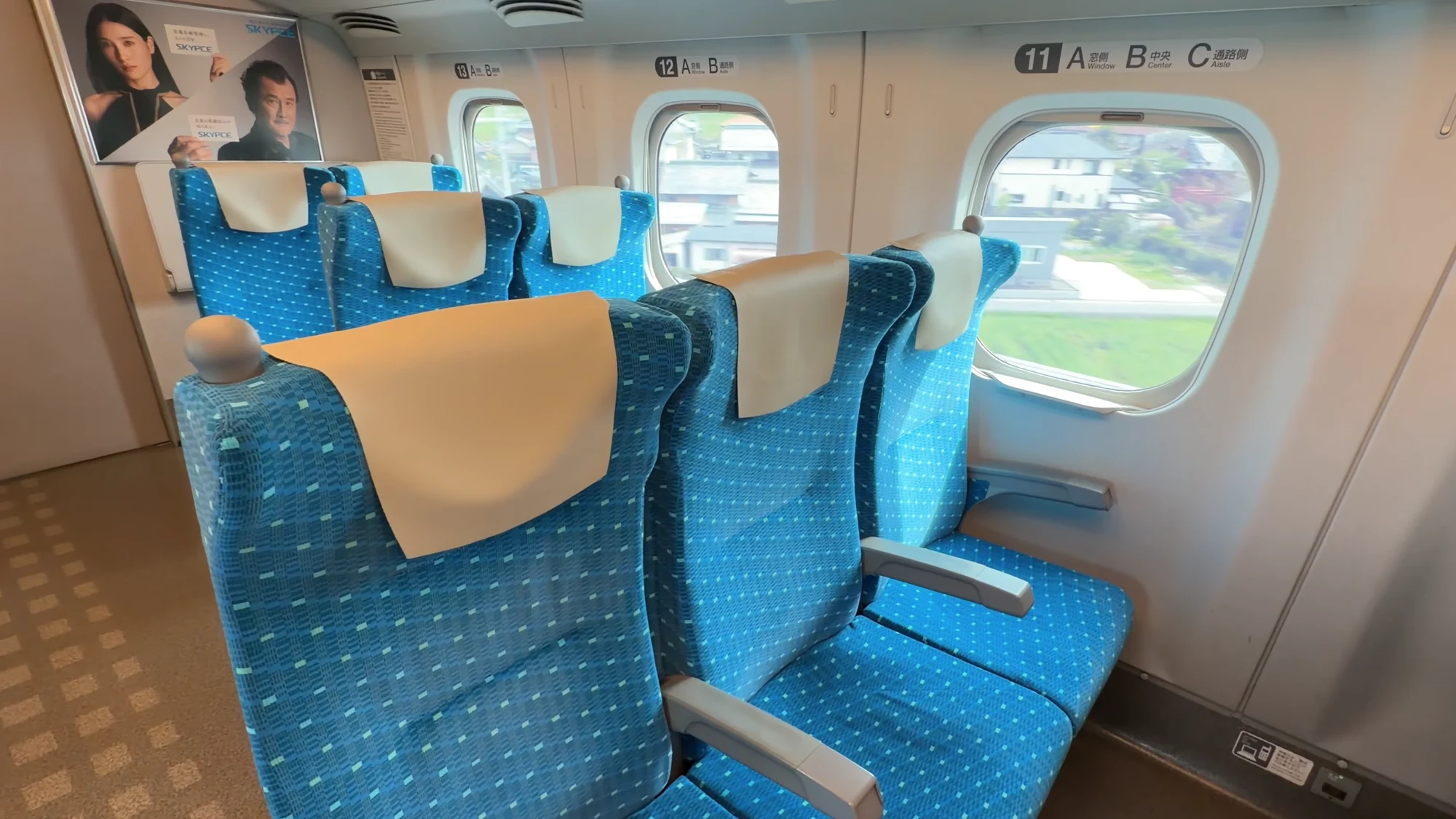 Blue reclining seats beside a wide train window with countryside passing outside.