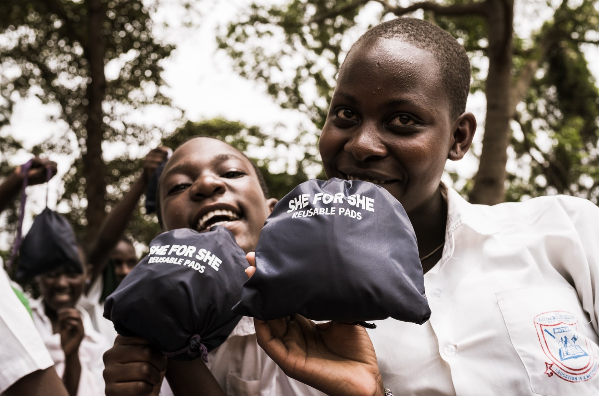 Two girls smiling while holding SHE FOR SHE reusable menstrual pads.