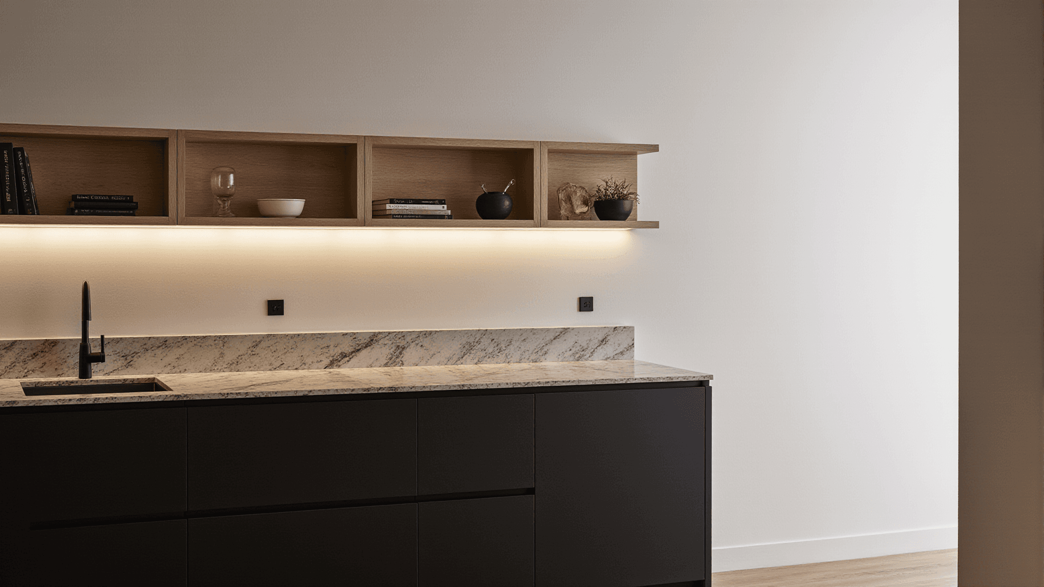 Minimal kitchen with marble countertop, dark cabinets, and open wooden shelves under soft lighting.