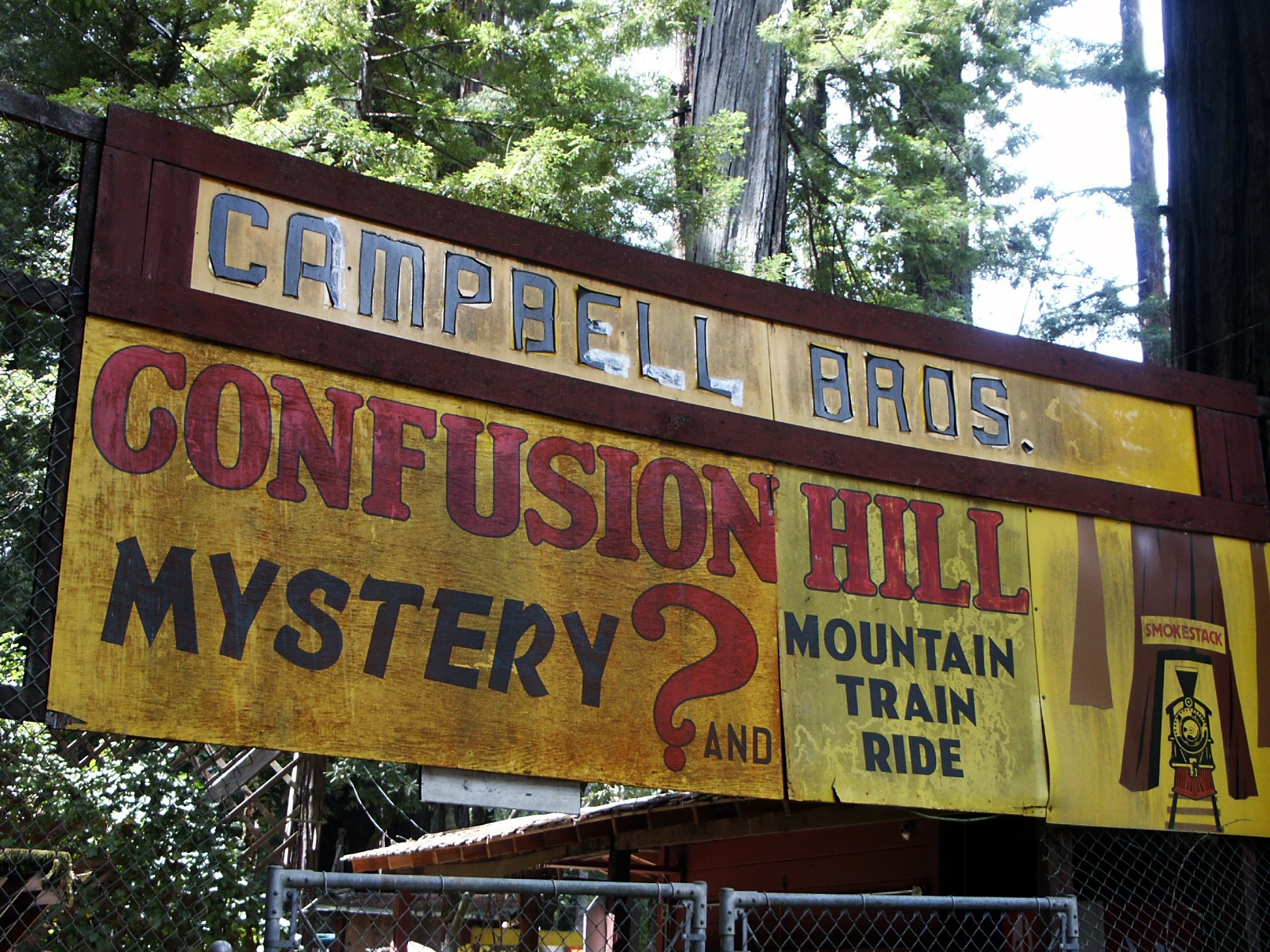 The colorful Confusion Hill entrance sign among redwood trees.