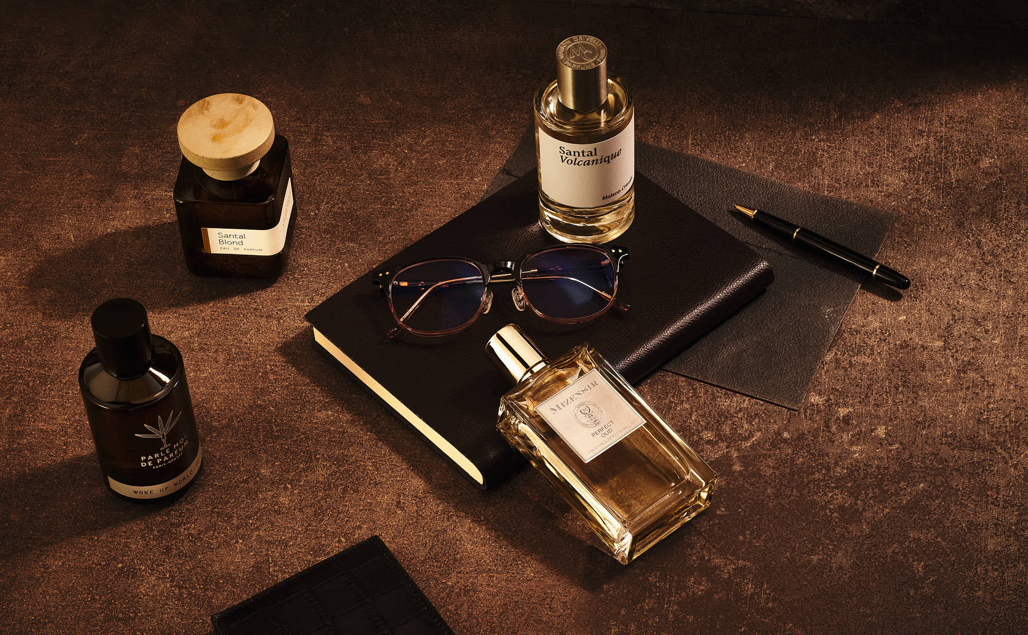 Luxury fragrances and accessories on a leather notebook with glasses and pen.