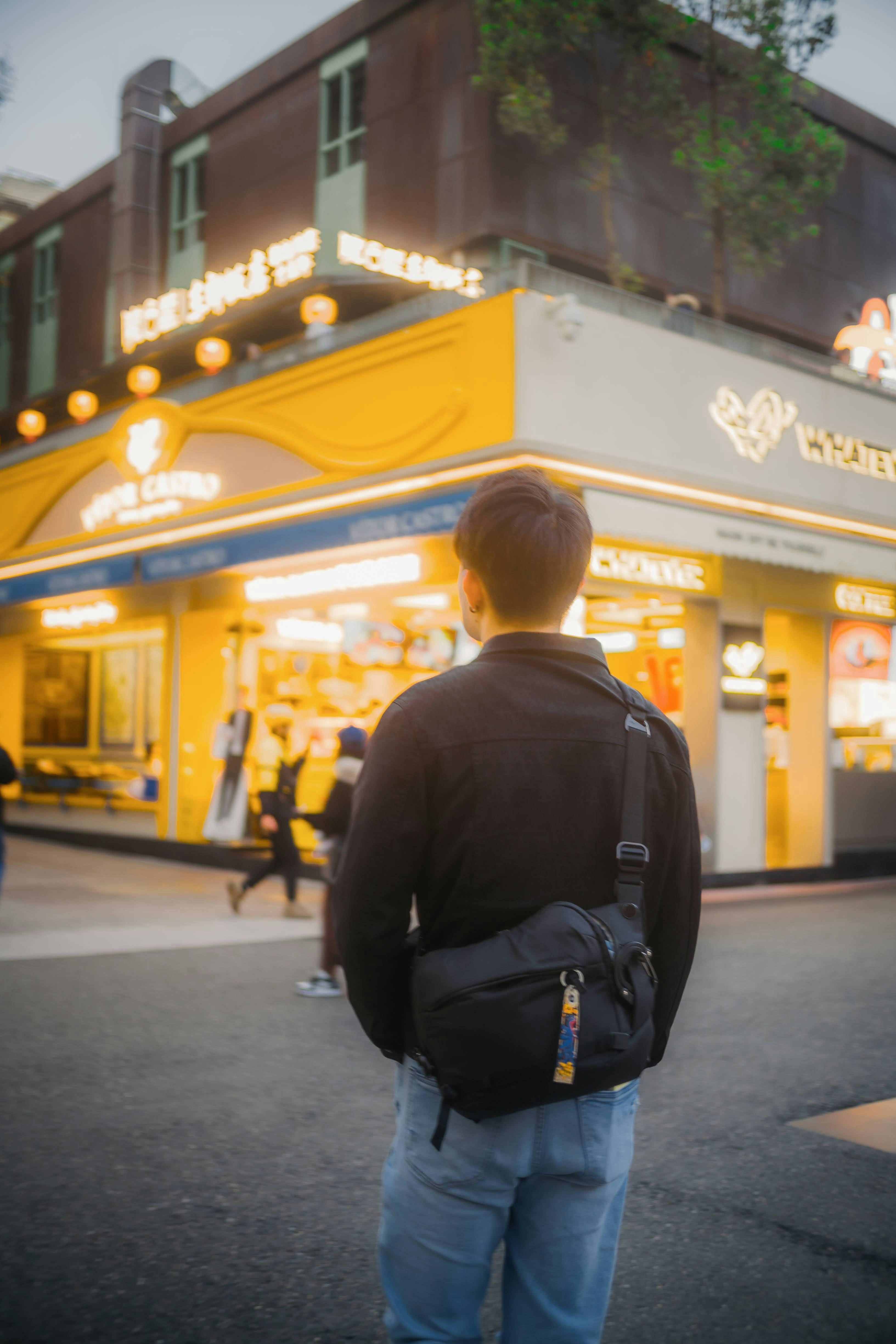 Man with a crossbody bag looking at a yellow building.