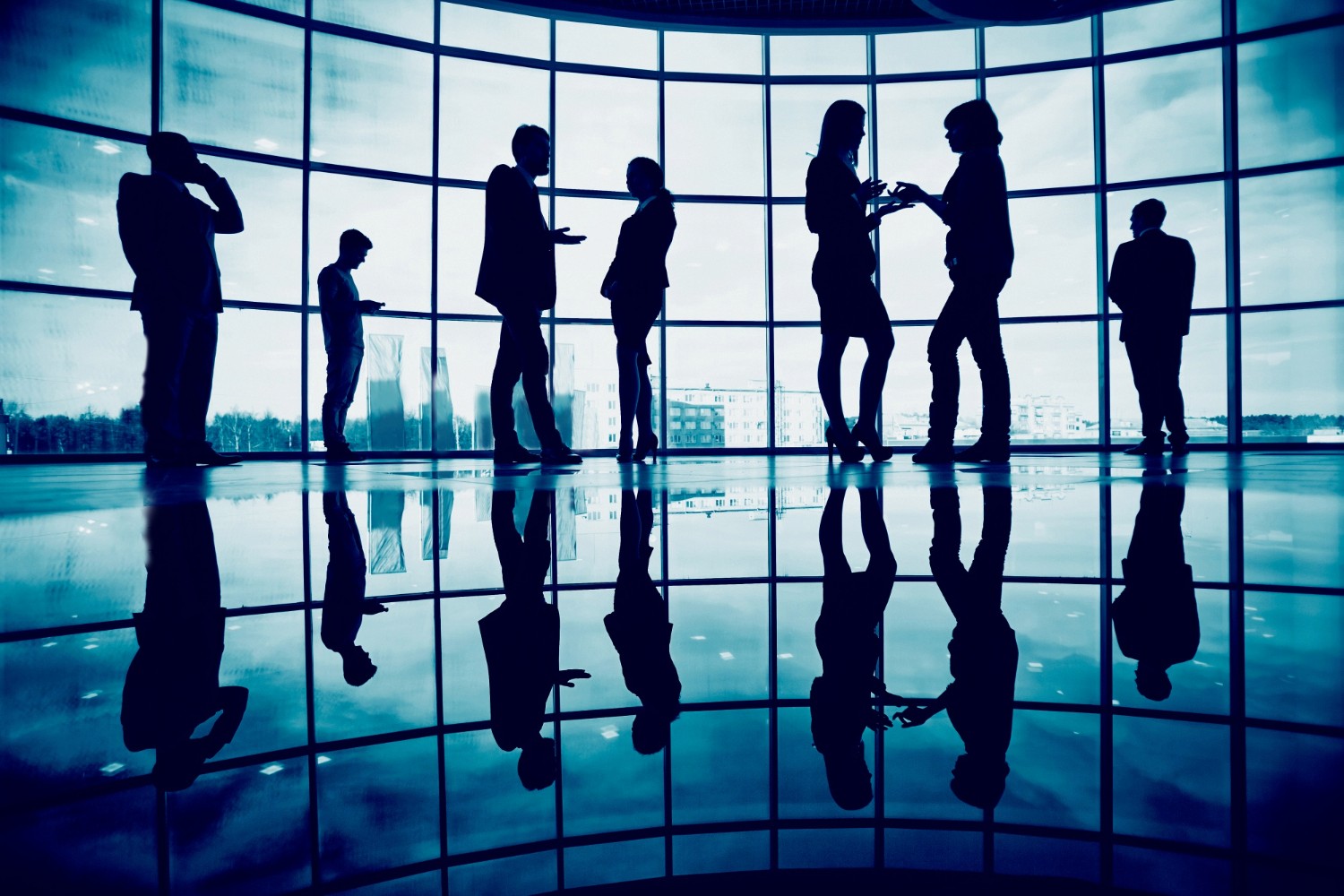 A young person with curly hair smiles at the camera while sitting in front of a laptop against a dark background.