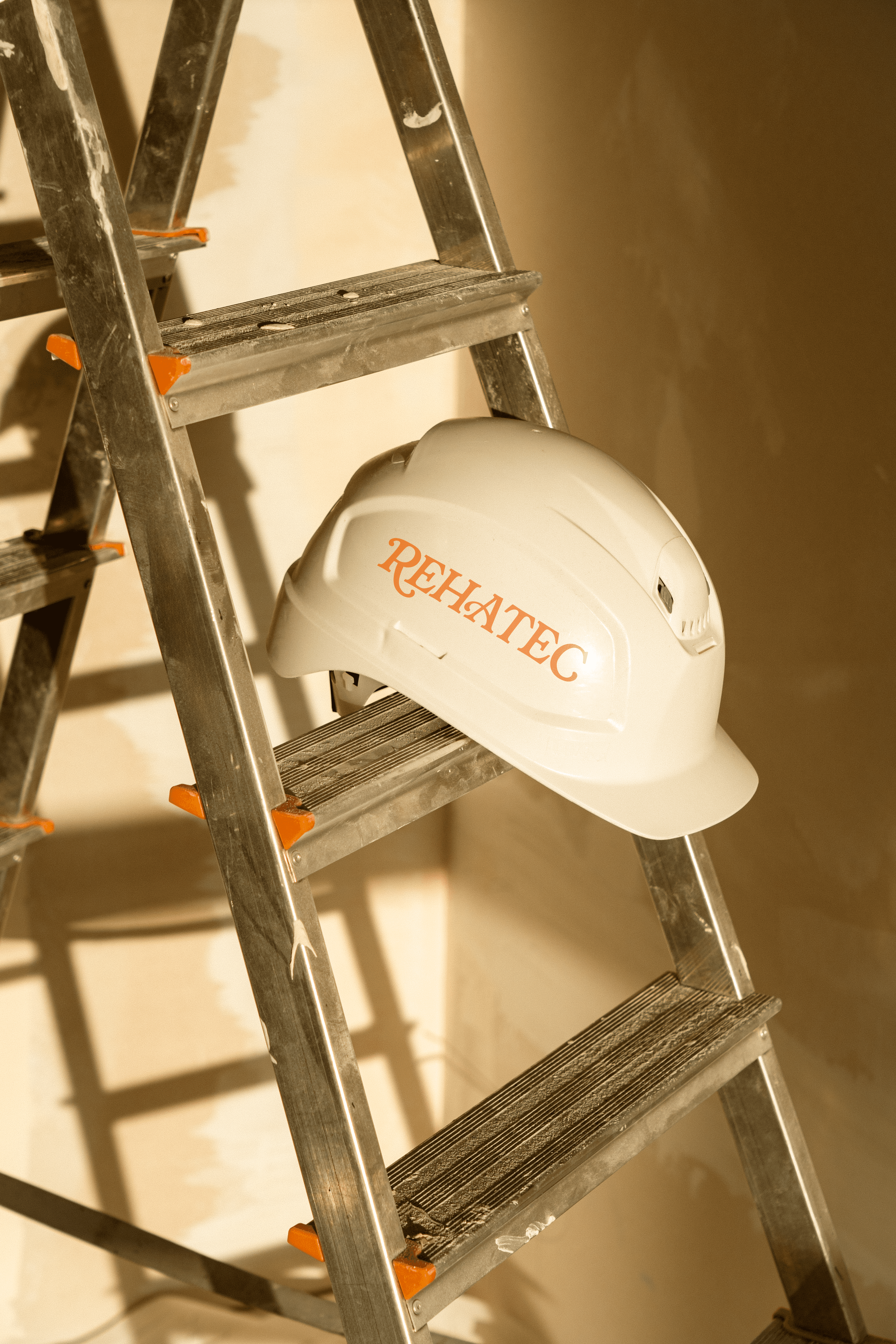 Casc d'obra amb el logo de Rehatec a sobre d'una escala metàl·lica