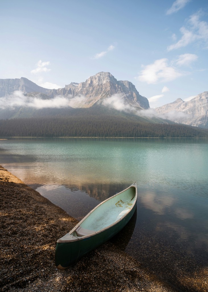 A canoe sitting by the end of a lake with a mountain in the background