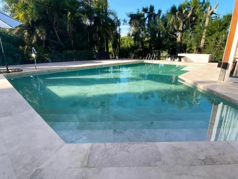 Construcción de piscina exterior rodeada de naturaleza, destacando una amplia escalera de acceso revestida en mármol travertino.