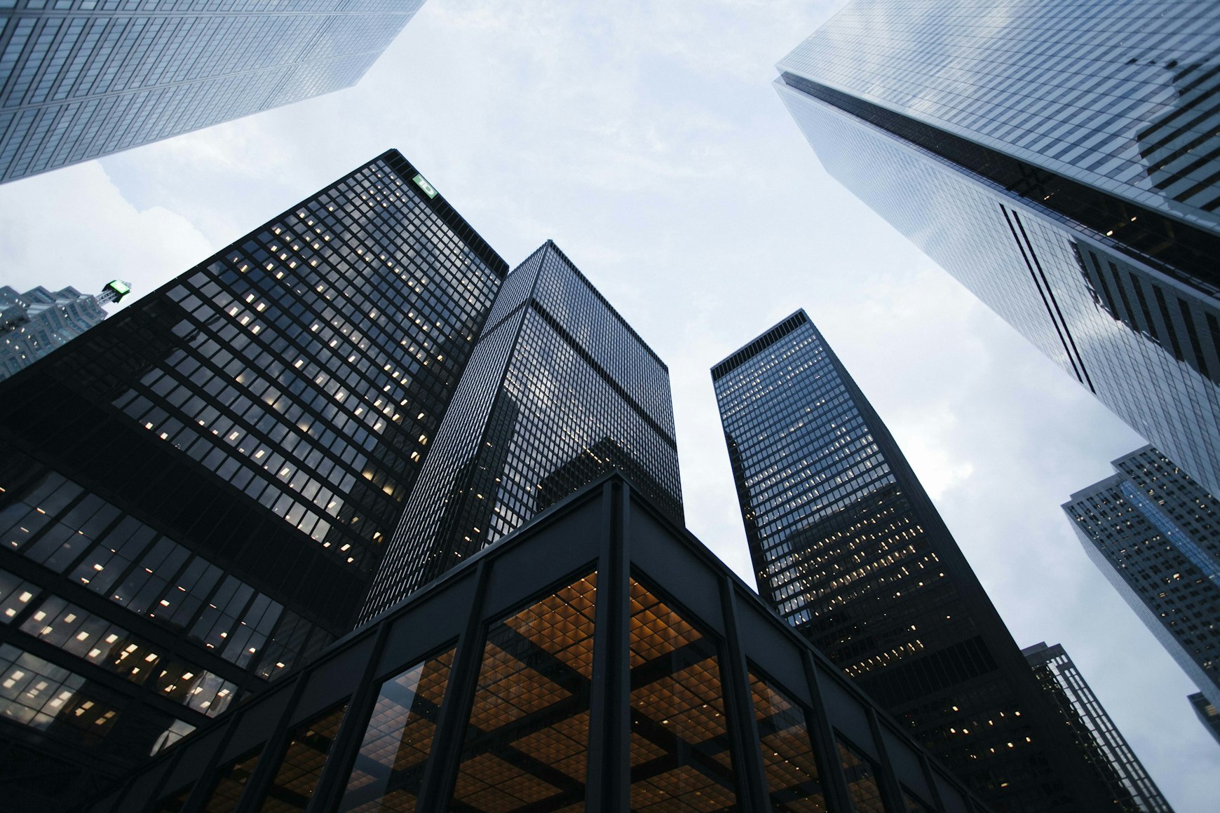 Low-angle view of tall glass and steel skyscrapers rising against an overcast sky.