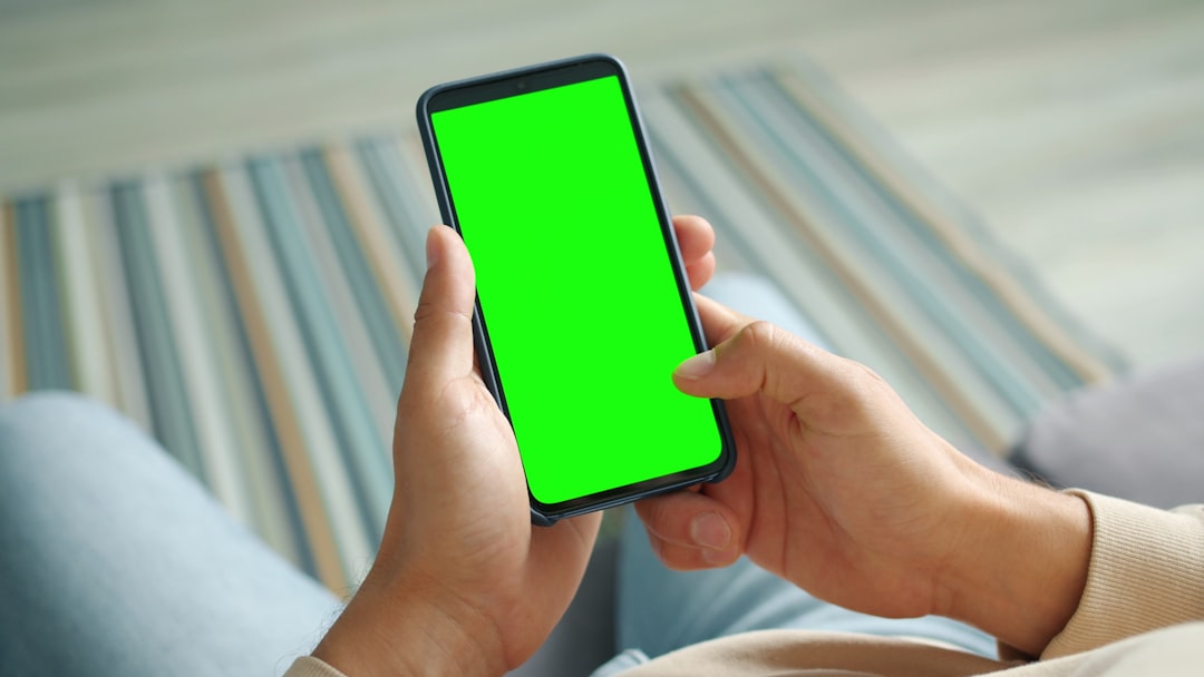Hands holding a smartphone with a green screen.