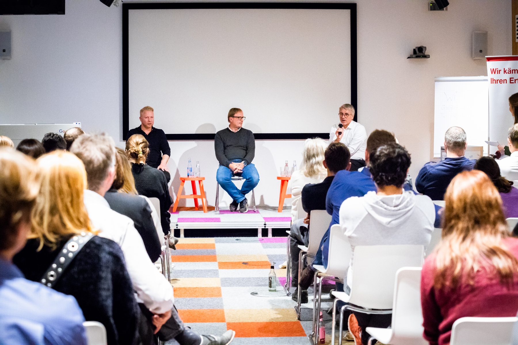 Drei Redner halten einen Vortrag auf einer Online-Marketing-Konferenz, während die Teilnehmer*innen interessiert zuhören - internetwarriors GmbH