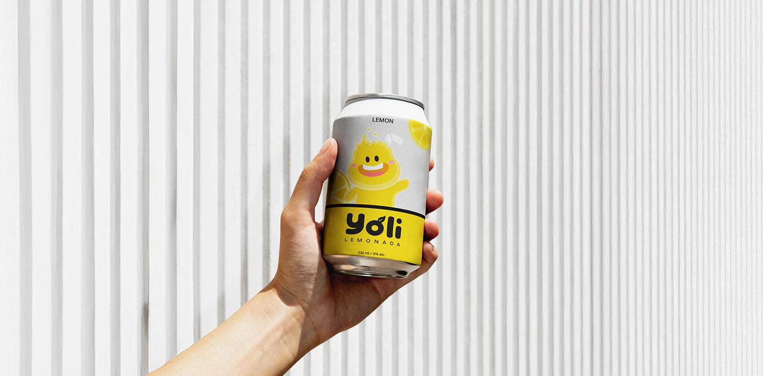 A hand holding a yellow Yoli lemonade can in front of a clean, minimal white background.